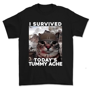 May include: Black t-shirt featuring a cat wearing a military helmet, with the text "I SURVIVED TODAY'S TUMMY ACHE." The cat graphic is set against a backdrop of a battlefield scene with smoke and explosions.