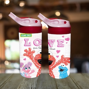 Op de afbeelding: Twee waterflessen met rode en roze details. De flessen tonen Sesamstraat-personages en het woord "LOVE" in roze. Eén fles heeft Abby Cadabby en Elmo, en de andere heeft Elmo en Koekiemonster. De flessen hebben een roze klapdeksel.