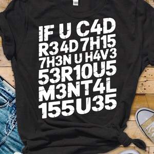 Könnte beinhalten: Schwarzes T-Shirt mit weißem Text: "IF U C4D R34D 7H15 7H3N U H4V3 53R10U5 M3NT4L 155U35". Das Shirt wird mit blauen Jeans und beigen Turnschuhen auf Holzgrund gezeigt.
