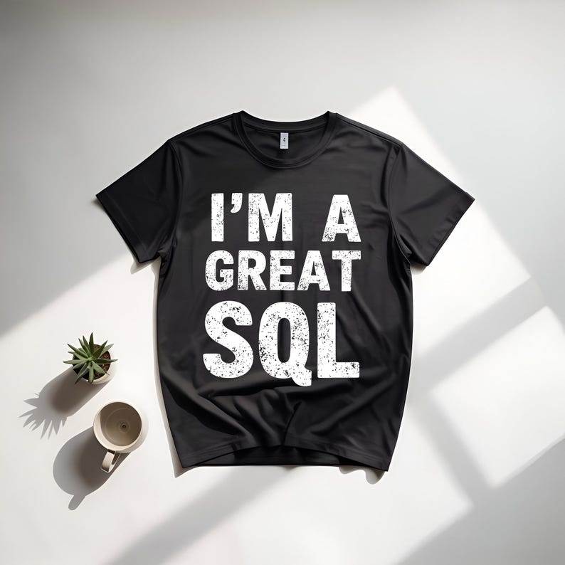May include: Black crew neck t-shirt with the white text "I'M A GREAT SQL". The shirt is displayed on a white surface with a small potted plant and a mug.