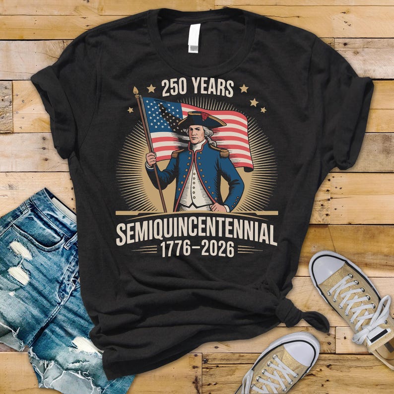 K&ouml;nnte beinhalten: Schwarzes T-Shirt mit einem Vintage-Grafik eines Mannes in einem blauen Mantel, der eine amerikanische Flagge h&auml;lt. Der Text "250 YEARS" steht &uuml;ber dem Bild und "SEMIQUINCENTENNIAL 1776-2026" darunter. Das Design feiert ein Jubil&auml;um.