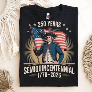 K&ouml;nnte beinhalten: Schwarzes T-Shirt mit einer Grafik zum 250. Jahrestag der Vereinigten Staaten. Das Design zeigt eine Illustration einer historischen Figur, die die amerikanische Flagge h&auml;lt, mit dem Text "250 YEARS SEMIQUINCENTENNIAL 1776-2026".