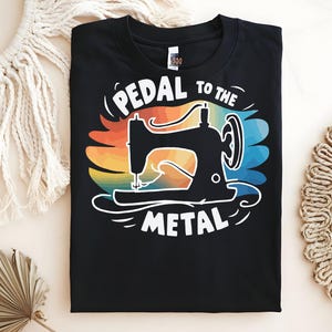 Puede incluir: Camiseta negra con un diseño de máquina de coser y el texto "PEDAL TO THE METAL". El diseño incluye un fondo degradado arcoíris. Un regalo ideal para los entusiastas de la costura y las manualidades.