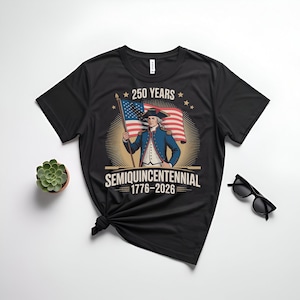 K&ouml;nnte beinhalten: Schwarzes T-Shirt mit einer Grafik eines Mannes, der eine amerikanische Flagge h&auml;lt, mit dem Text "250 Years Semiquincentennial 1776-2026." Das Design beinhaltet Sterne und einen Sonnenstrahleffekt, der ein historisches Ereignis feiert.