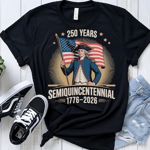 K&ouml;nnte beinhalten: Schwarzes T-Shirt mit einer Grafik zum 250. Jahrestag der Vereinigten Staaten. Das Design zeigt eine koloniale Figur, die eine amerikanische Flagge h&auml;lt, mit dem Text "250 Years Semiquincentennial 1776-2026."