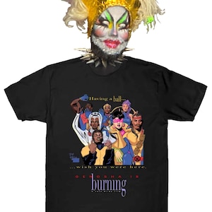 May include: Black t-shirt with a graphic of a group of cartoon characters. The text "Having a ball... wish you were here." is printed on the shirt. The text "GENOSHA IS BURNING" is printed below the graphic.