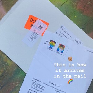May include: A white envelope with a "Do Not Bend" sticker and a packing list for two prints. The packing list includes the order number, the seller's information, the shipping address, and the expected delivery date. The text "This is how it arrives in the mail" is written on the envelope with a rainbow emoji and a raised fist emoji.