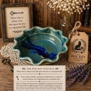 May include: A scalloped-edge ceramic bowl with a teal and deep blue glaze. The bowl is accompanied by a brown paper tag featuring a fox illustration and the text The Fox Key Cottage, a small metal skeleton key, and a sprig of dried lavender.