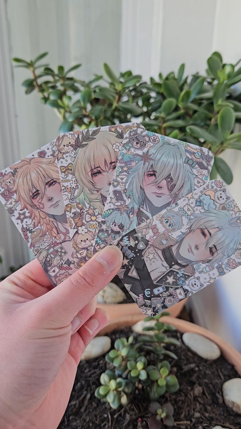 Four front-facing photocards held to the camera. Each card is an illustration of a honkai star rail amphoreus character. From left to right is: Mydei, Aglaea, Anaxa and Phainon.
