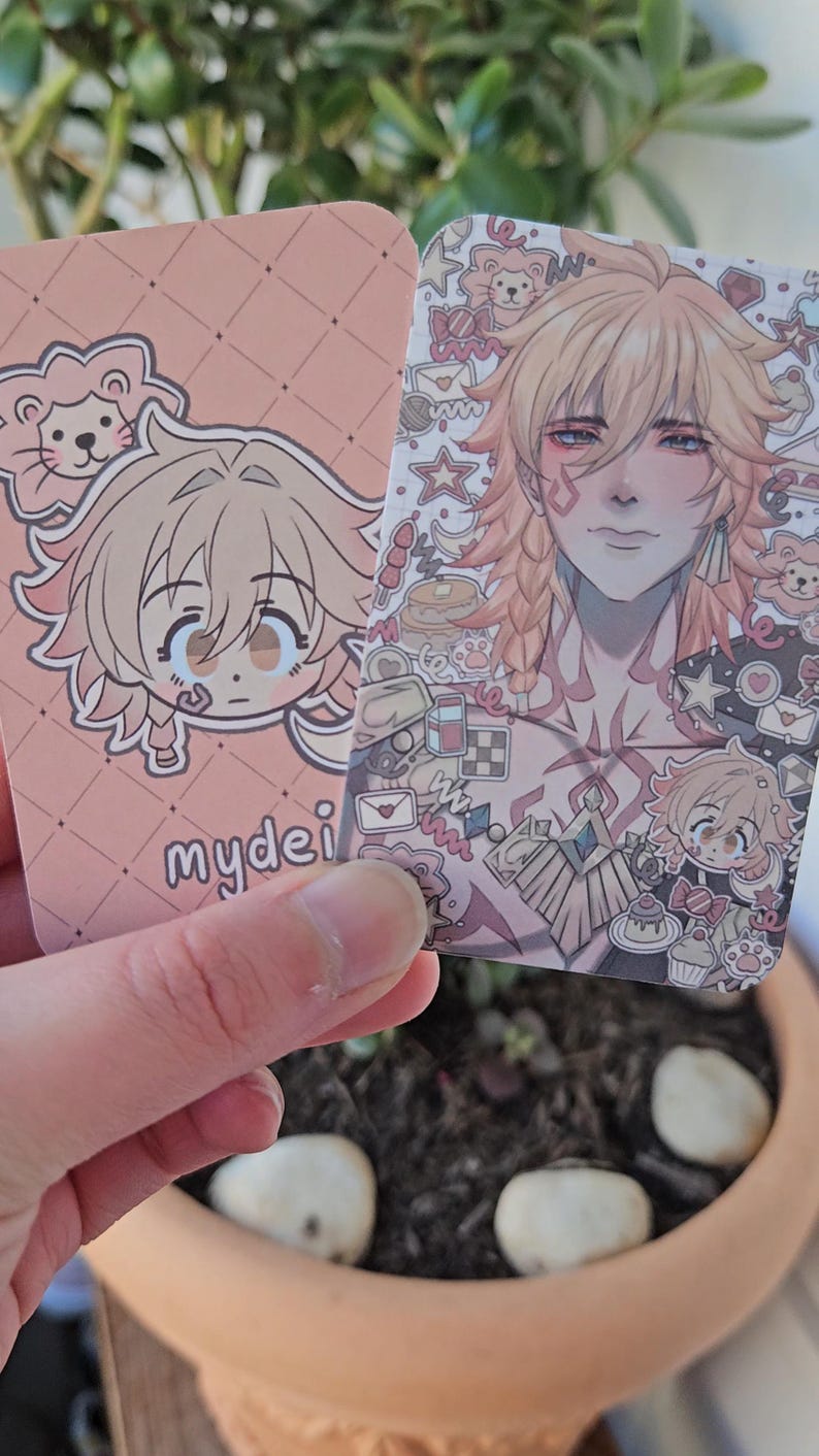 Two of the same photocard are shown. One to display the back-faced card, while the other displays the front face of the card. It is of the character Mydei from honkai star rail. The back-face contains a chibi version of the character while the front is a more detailed illustration of said character decorated with stickers all around them.