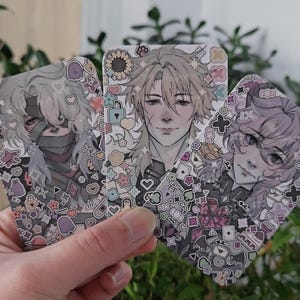 Puede incluir: Tres tarjetas ilustradas con retratos de estilo anime. Cada tarjeta presenta un personaje diferente con peinados y rasgos faciales distintivos. Las tarjetas están decoradas con pequeñas formas y símbolos coloridos y estampados.