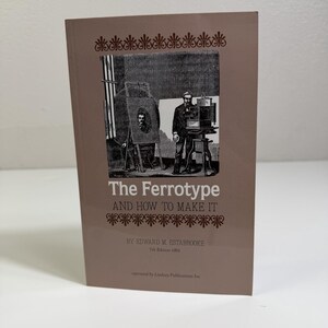 May include: A soft brown paperback book titled The Ferrotype AND HOW TO MAKE IT by Edward M. Estabrooke, 7th Edition 1891, reprinted by Lindsay Publications Inc. The cover features a black and white illustration of a photographer with a camera.
