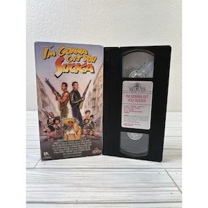 Op de afbeelding: Een VHS-band van de film "I'm Gonna Git You Sucka" met de hoes open. De hoes toont een kleurrijke filmposter met acteurs die wapens vasthouden. De band is zwart met een wit label.