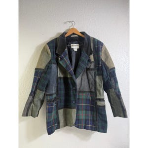 May include: A patchwork blazer featuring alternating panels of dark green and blue plaid fabric alongside solid olive green sections. The garment includes a notched lapel, two front buttons, and two lower pockets, all constructed with a visible seam design.
