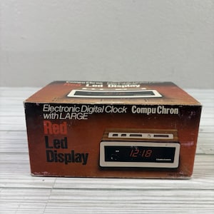 以下が含まれることがあります： 赤色LEDディスプレイを備えた、ヴィンテージのCompuChron電子デジタル時計。 時計は木目調のケースに収められており、時刻は午前12時18分と表示されています。 箱には「Electronic Digital Clock CompuChron with LARGE Red Led Display」と書かれています。