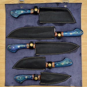May include: Set of five kitchen knives with blue and black handles and leather sheaths. The knives are arranged in a row on a blue background.