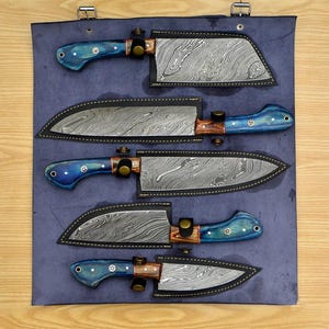 May include: Set of four kitchen knives with blue and brown handles, displayed in a blue leather roll with individual slots for each knife. The knives have a Damascus steel blade pattern.