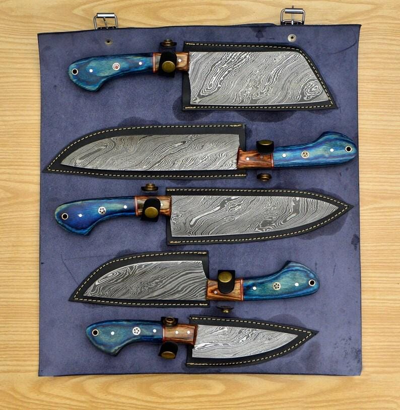 May include: Set of four kitchen knives with blue and brown handles, displayed in a blue leather roll with individual slots for each knife. The knives have a Damascus steel blade pattern.