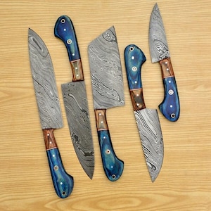 May include: Set of five kitchen knives with blue and brown handles and a patterned blade. The knives are arranged in a row on a wooden surface.