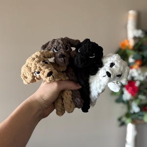 May include: Four crocheted dog toys in different colors: brown, black, white, and beige. The toys are made with a soft, fluffy yarn and have cute, embroidered faces.