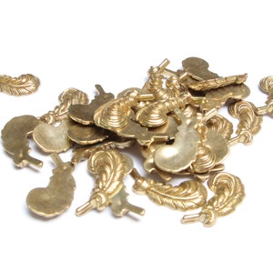 May include: A collection of small, gold-colored feather charms. The charms have detailed feather designs and are scattered on a white surface. These charms are suitable for jewelry making or craft projects.