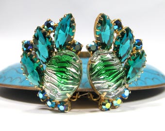 May include: Vintage clip-on earrings with a gold-tone setting. Each earring features a large, oval-shaped green and silver stone, surrounded by teal and dark blue teardrop-shaped and round crystals. A unique jewelry piece.