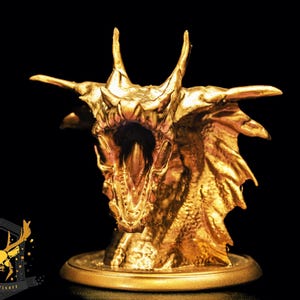Peut inclure: Une sculpture de dragon doré avec une gueule ouverte, des dents acérées et des écailles détaillées. Le dragon a de grandes cornes et des ailes, sur fond noir. La sculpture est sur une base ronde.