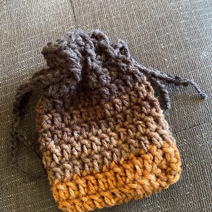 May include: A small crocheted drawstring bag with a brown, dark brown, and orange ombre color pattern.