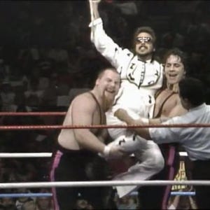 Könnte beinhalten: Eine Wrestling-Szene mit mehreren Wrestlern in einem Ring. Ein Wrestler in einem weißen Outfit mit schwarzen Details und Sonnenbrille wird von zwei anderen hochgehalten. Die Wrestler tragen schwarze und rosa Shorts.