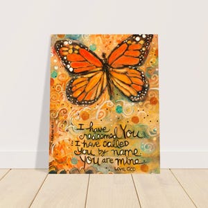 Puede incluir: Una impresión de arte colorida con una mariposa y el texto "Te he redimido. Te he llamado por tu nombre. Eres mío. Amor, Dios."
