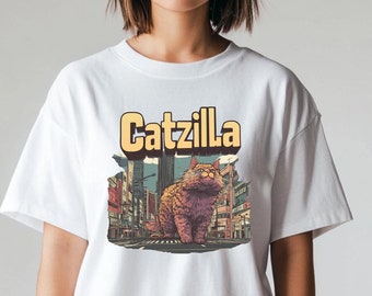 May include: White t-shirt with a graphic of a large orange cat with the text "Catzilla" above it. The cat is standing in a city street with tall buildings in the background.