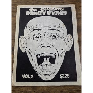 May include: A rectangular book cover titled The Complete Monty Python Vol. 2 with a price of $225. The cover features a high-contrast black and white illustration of a bald head with a wide-open mouth containing a pair of feet inside the throat.