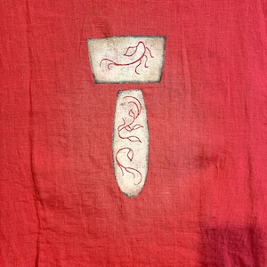 May include: A vibrant red garment featuring a textured fabric surface. Centered on the fabric are two distinct off-white shapes with dark, distressed edges. The top shape is trapezoidal and the bottom is oval, both containing red line art designs.