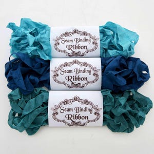 May include: Three spools of seam binding ribbon in shades of teal, blue, and turquoise. Each spool is labelled "Seam Binding Ribbon" in a brown font.