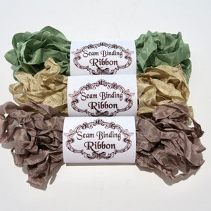 May include: Three spools of seam binding ribbon in green, beige, and brown. Each spool has a white label with the text "Seam Binding Ribbon" in brown lettering.