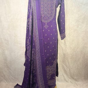May include: A purple long-sleeved dress with a gold geometric pattern. The dress has a matching dupatta with a similar pattern.