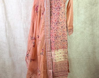 May include: A peach-colored salwar kameez with a floral print and gold embroidery. The set includes a long-sleeved top, pants, and a matching dupatta.