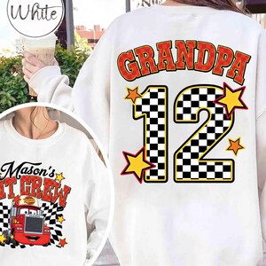 K&ouml;nnte beinhalten: Wei&szlig;es Sweatshirt mit dem Wort "GRANDPA" in roter und gelber Schrift und der Zahl "12" in einem schwarz-wei&szlig;en Schachbrettmuster. Gelbe Sterne umgeben die Zahl. Ein zweites Sweatshirt zeigt den Text "Mason's IT CREW" mit einem Cartoon-Truck.