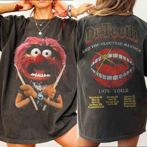Könnte beinhalten: Dunkelgraues T-Shirt mit einem Aufdruck von Animal von den Muppets, der Schlagzeug spielt. Auf der Rückseite des Shirts steht "Dr. Teeth and the Electric Mayhem 1976 Tour" mit einer Mundgrafik.