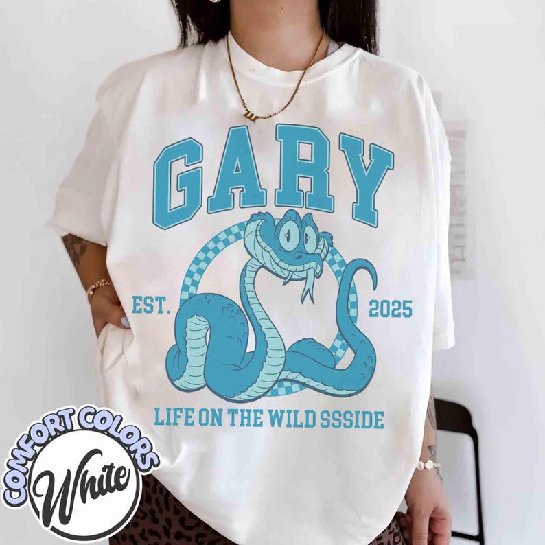 May include: White t-shirt with a blue snake graphic and the word "GARY" in a collegiate font. The design includes the text "EST. 2025" and "LIFE ON THE WILD SSSSIDE". The shirt is from Comfort Colors.