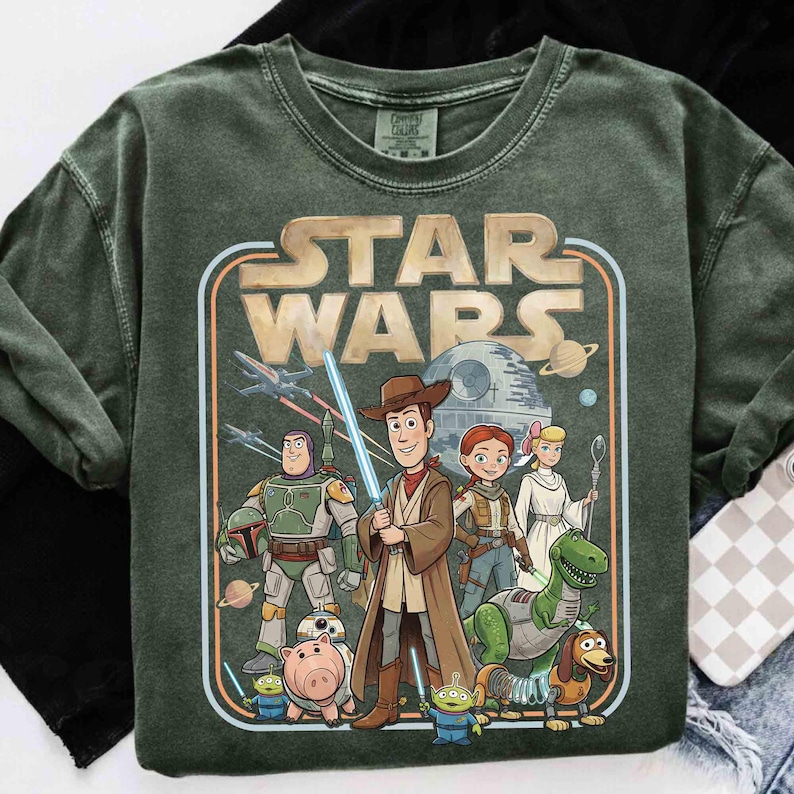 Puede incluir: Sudadera verde oscuro con un gr&aacute;fico de Star Wars con personajes de Toy Story. El dise&ntilde;o incluye a Woody, Buzz Lightyear y otros personajes, con el logo de Star Wars en un estilo retro.