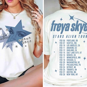 May include: Cream-colored t-shirt featuring a blue star graphic with the text "Silent Treatment" and "FREYA SKYE." The back of the shirt displays "freya skye STARS ALIGN TOUR" and a list of tour dates and locations.