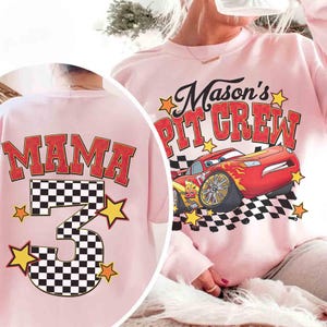 K&ouml;nnte beinhalten: Hellrosa Sweatshirt mit dem Aufdruck "Mason's Pit Crew" und einer Cartoon-Rennwagen-Grafik. Auf der R&uuml;ckseite steht "Mama" und die Zahl "3" mit Schachbrettmuster und Sternen. Ein lustiges, thematisches Kleidungsst&uuml;ck.