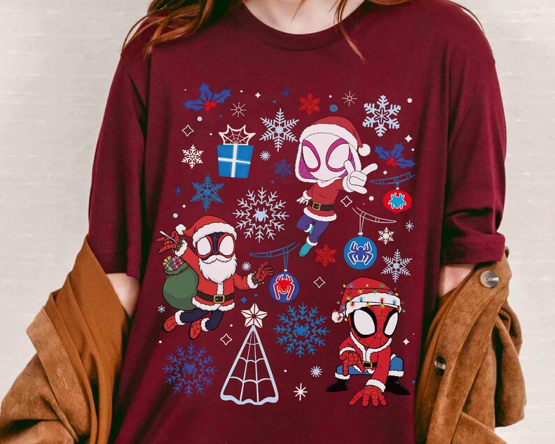 May include: Burgundy long-sleeve shirt featuring a festive design with Spider-Man characters in Santa Claus outfits. The graphic includes snowflakes, ornaments, and a Christmas tree. The shirt is a comfortable, casual wear.