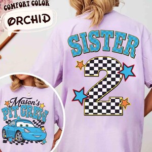 K&ouml;nnte beinhalten: Ein helllila T-Shirt mit dem Wort "SISTER" in blauen Buchstaben mit gr&uuml;nem Umriss und einer karierten Zahl 2. Auf der Vorderseite des Shirts steht der Text "Mason's Pit Crew" und ein blaues Cartoon-Auto.