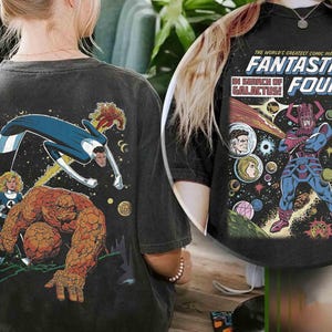 Può includere: T-shirt grigio scuro con arte a fumetti dei Fantastici Quattro. Il retro della maglietta mostra un'illustrazione colorata della squadra in azione, con il testo "Fantastic Four" e "In Search of Galactus!" stampato sopra una scena cosmica.