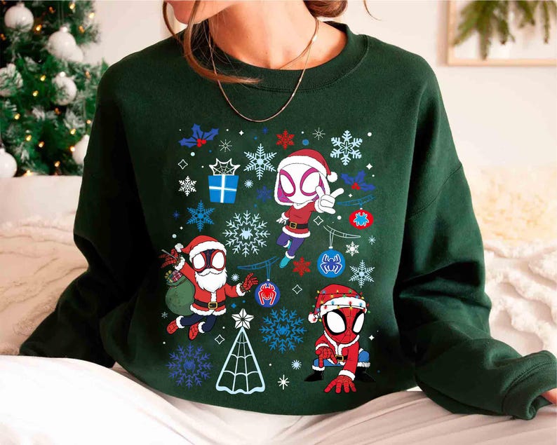 May include: Dark green sweatshirt featuring a festive design with cartoon Spider-Man characters in Santa hats. The graphic includes snowflakes, ornaments, and a Christmas tree. The design is set against a dark green background.