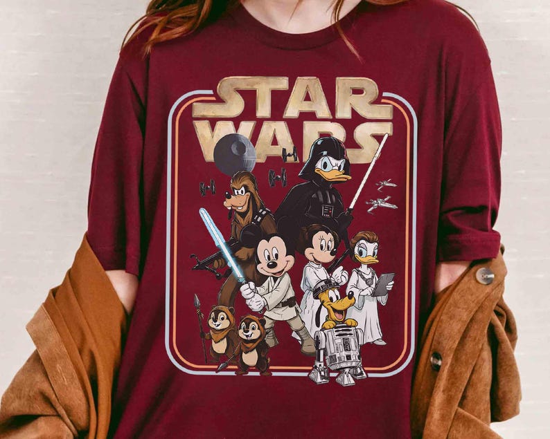 Puede incluir: Camiseta burdeos con el logo de Star Wars en un dise&ntilde;o retro. El gr&aacute;fico incluye varios personajes de Disney disfrazados de personajes de Star Wars, como Mickey Mouse como Luke Skywalker y Donald Duck como Darth Vader.