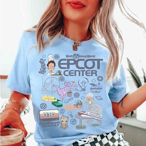 Peut inclure: T-shirt bleu clair avec un motif graphique color&eacute;. Le motif comprend le texte "Walt Disney World Epcot Center" et des illustrations de personnages et d'ic&ocirc;nes du parc &agrave; th&egrave;me, comme R&eacute;my de Ratatouille et Figment.