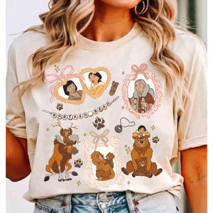 Pode incluir: Camiseta creme com ilustrações de desenhos animados do filme "Irmão Urso". O design inclui retratos emoldurados de personagens, ursos e o texto "Brother Bear". Pegadas e estrelas também estão incluídas.